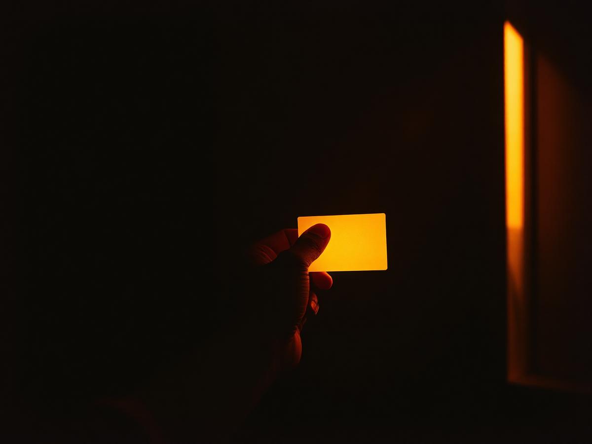 A hand holding a small warm-lit card in a dark room